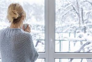 一个穿着舒适毛衣的女人站在观景窗前，手里拿着一杯饮料